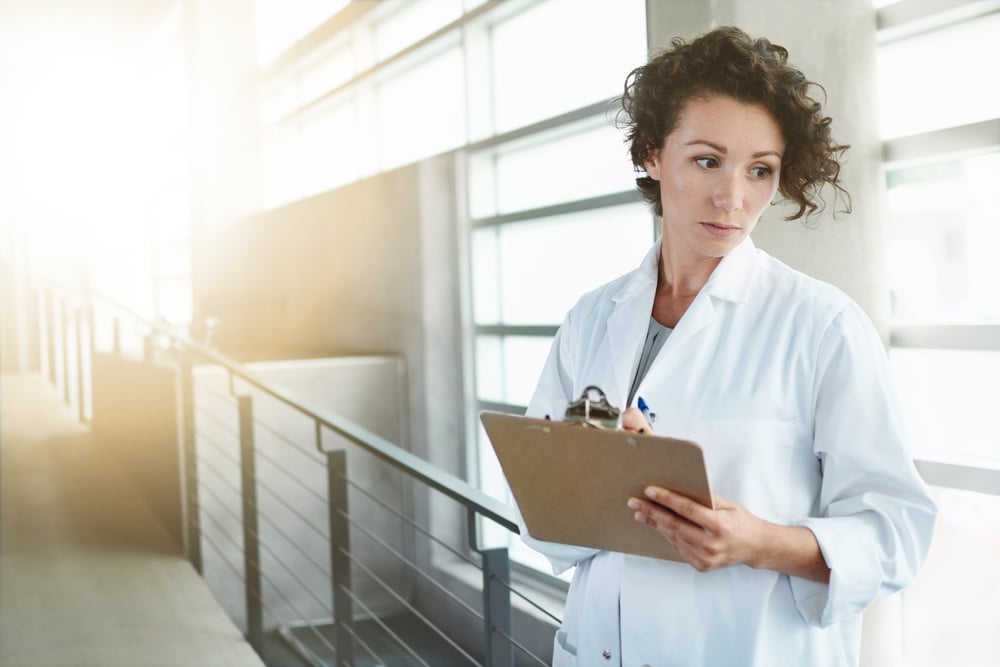 Portrait of a serious female doctor holding her patient chart in bright modern hospital